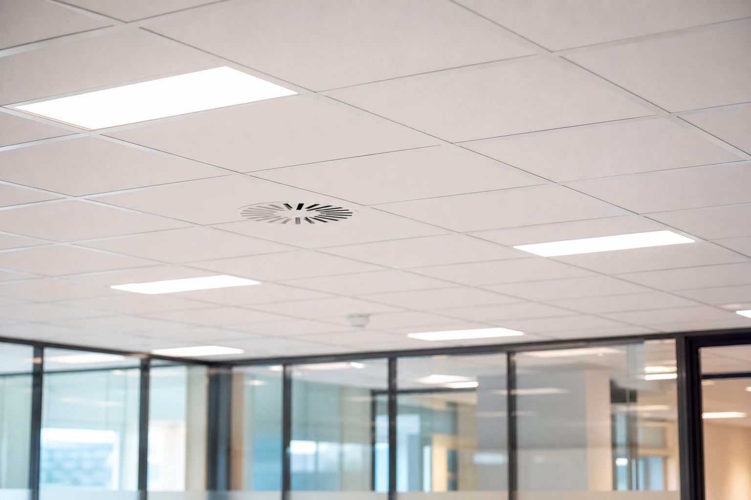 Nedsenket systemhimling med integrerte lyspaneler og ventilasjonsventil over glassvegger i kontorlokale